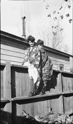 Two women in kimono-style wraps astride fence