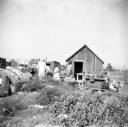 Paiute Indians standing among their belongings in front of a house