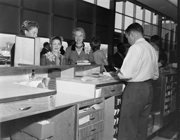 Three women at a counter with a man behind it assisting them, 2