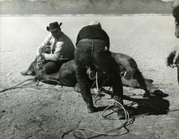 Two men roping horse on ground