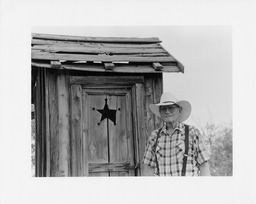 Lawrence Marshall beside outhouse, Logandale