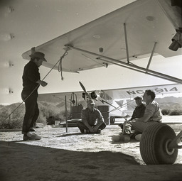 Men under plane wing, plane in background