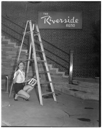 Diane Schindler under a ladder with a Friday the 13th calendar page in front of 'The Riverside Reno' sign
