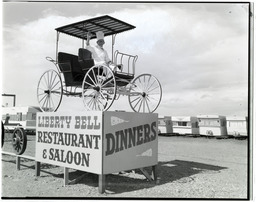 A man on a raised wagon with sign for Liberty Bell Restaurant & Saloon