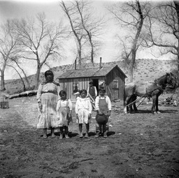 A Paiute woman, man, and children standing in front of a house