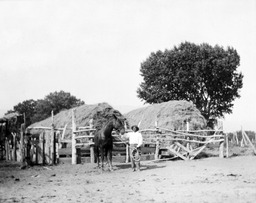 Man with horse in front of corral