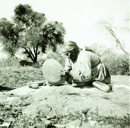 Indian woman with basket tray, grinding in bedrock mortar