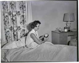 A woman in a nightgown in bed holding an alarm clock