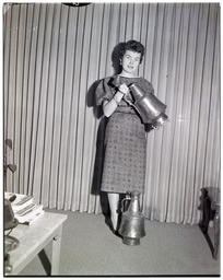 A woman modeling a metal jug, with an identical one on the floor