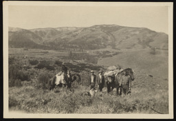 Men, horses, and a dog on a hillside in front of a valley