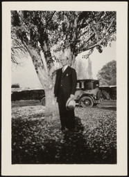 Dr. Church with hat in hand standing in front of tree
