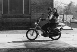 Students on campus, riding a moped, 1980